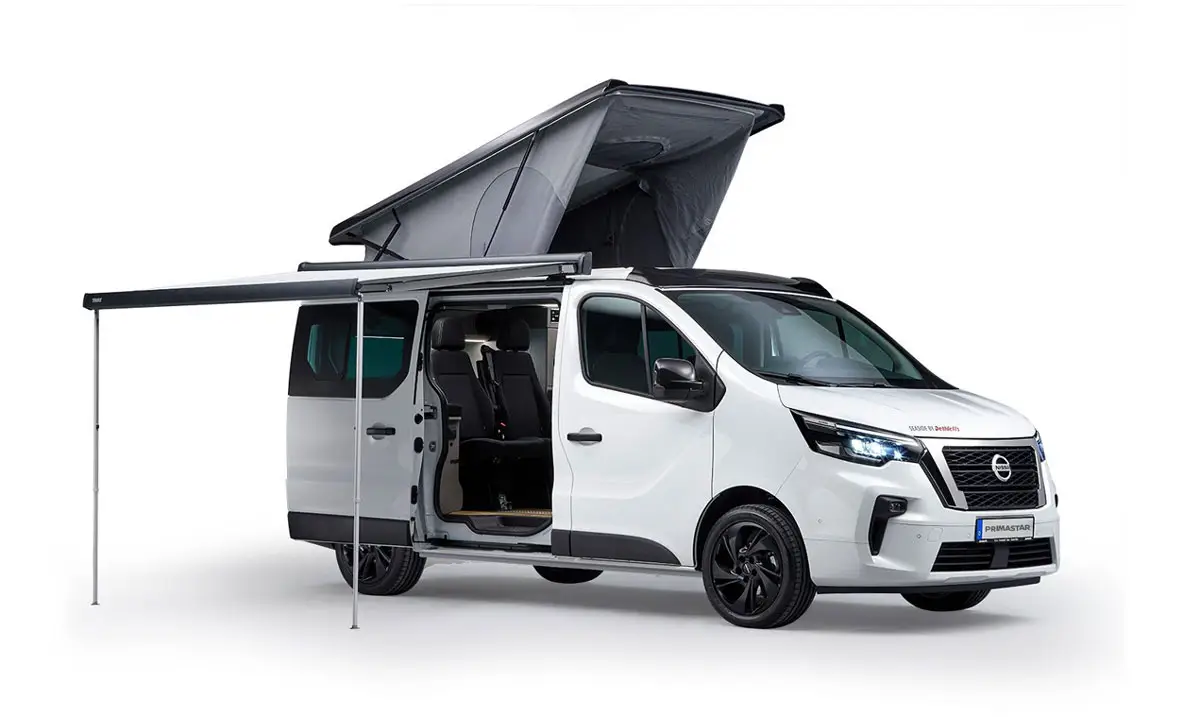 Nissan Primastar Dethleffs &ndash; wei&szlig;es Campingfahrzeug mit Aufstelldach, ge&ouml;ffneter T&uuml;r und Markise.